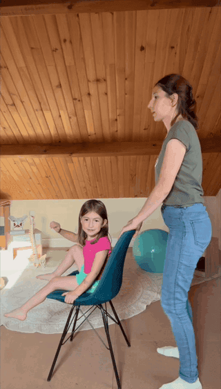 Une enfant assise sur une chaise et une adulte qui l’accompagne pendant un exercice.